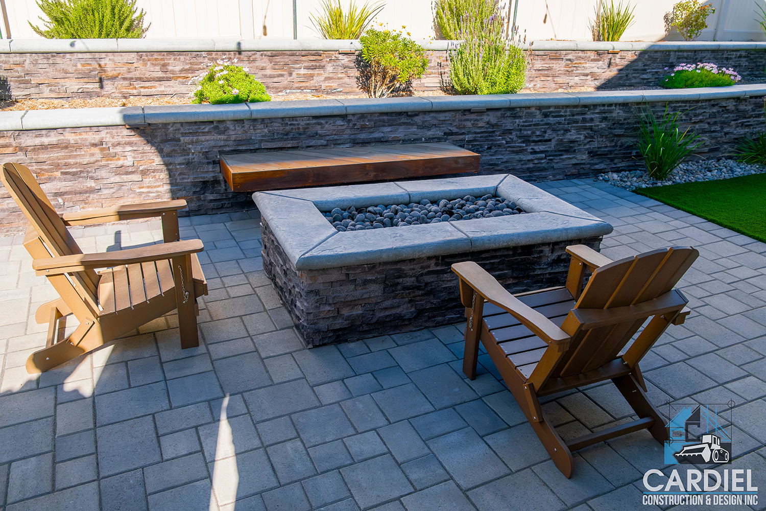 Revitalized backyard featuring lush turf, a cozy firepit, elegant pavers, a sturdy retaining wall, and vibrant plantings, creating a serene outdoor retreat.